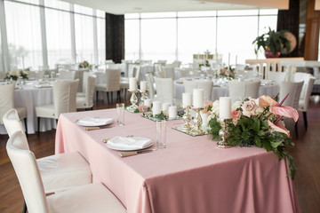 The wedding table setting for the newlyweds is decorated with fresh flowers of carnation, rose, anthurium and eucalyptus leaves. Silver candlesticks, white candles. Wedding floristry. Close-up details