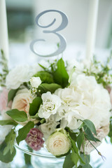 Wedding table setting is decorated with fresh flowers and white candles. Wedding floristry. Bouquet with roses, hydrangea and eustoma. Table numbering