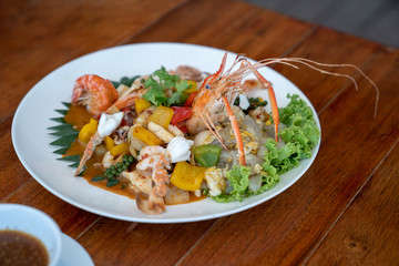 Seafood Thai mixxed together between boiled shrimp, crab, squid and colourful vegetable in dish on wood table in restaurant.