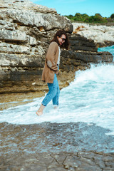 woman walking by rocky sea beach at sunny windy day. summer vacation
