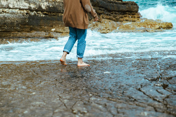 woman walking by rocky beach barefoot wet jeans - Powered by Adobe