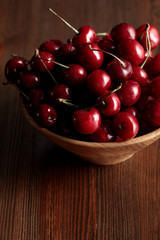 wooden bowl with red ripe cherries on wooden brown table