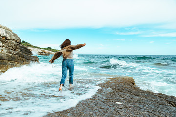 woman walking by rocky sea beach at sunny windy day. summer vacation