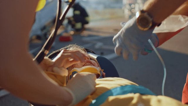 On the Car Crash Traffic Accident Scene: Paramedics Saving Life of a Traffic Accident Victim who is Lying on Stretchers. They Listen To a Heartbeat, Apply Oxygen Mask and Give First Aid Help