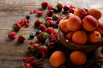 ripe delicious seasonal berries scattered around bowl with fresh apricots on wooden table