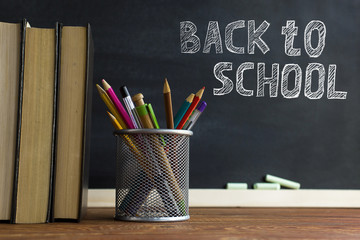 Textbooks and school supplies on a table, against a chalkboard background with chalk. Concept of school with copyspase.
