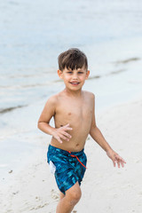 Little boy standing at the beach running out of the water