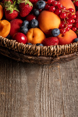 close up view of ripe seasonal berries and apricots in wicker basket on wooden table