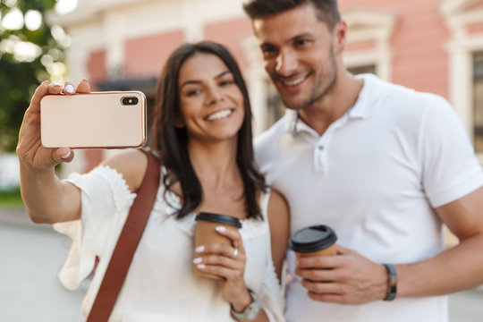 Portrait of stylish young couple taking selfie photo on smartphone while walking outdoors