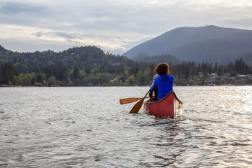 Couple adventurous female friends on a red canoe are paddling in the Howe Sound during a cloudy sunset. Taken near Bowen Island, West of Vancouver, BC, Canada.