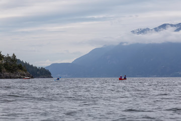 Adventurous friends on a red canoe and kayak are paddling in the Howe Sound during a cloudy sunset. Taken near Bowen Island, West of Vancouver, BC, Canada.
