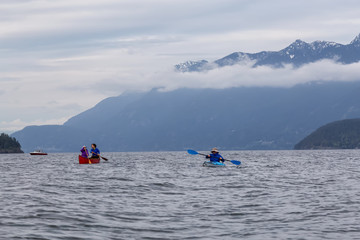 Naklejka premium Adventurous friends on a red canoe and kayak are paddling in the Howe Sound during a cloudy sunset. Taken near Bowen Island, West of Vancouver, BC, Canada.