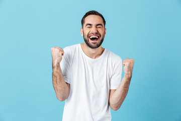Young screaming happy bearded man posing isolated over blue wall background make winner gesture.
