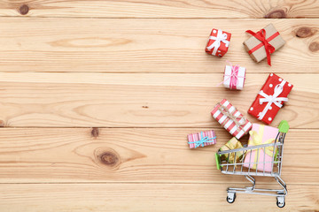 Small shopping cart with gift boxes on brown wooden table