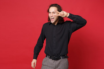 Handsome stylish young curly long haired man in black shirt posing isolated on red wall background studio portrait. People sincere emotions lifestyle concept. Mock up copy space. Looking camera smile.