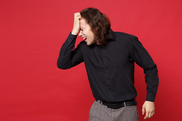 Young sad curly long haired man in black shirt standing posing isolated on red wall background studio portrait. People sincere emotions lifestyle concept. Mock up copy space. Problem crisis depression