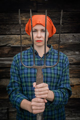 Young woman stands with a pitchfork near a stable on a ranch.