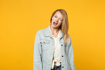 Portrait of attractive young woman in denim casual clothes standing, looking camera, blinking isolated on bright yellow orange wall background in studio. People lifestyle concept. Mock up copy space.