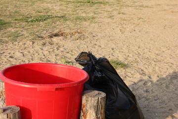 Plastic garbage collection tank and plastic garbage bag full of garbage nearby.