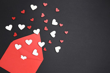 Red paper envelope with wooden hearts on black background