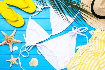 Fashion swimsuit with palm leaf and seashells on blue wooden table