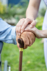 Nurse holding elderly man hand with cane on wheelchair in garden close up