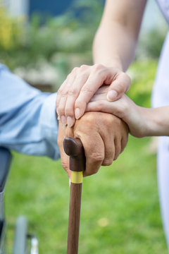 Nurse Holding Elderly Man Hand With Cane On Wheelchair In Garden Close Up