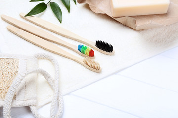 Bamboo toothbrushes with towel, washcloth and green leafs on white wooden table