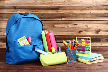 Backpack with school supplies on brown wooden table