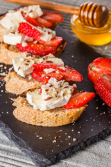 Bruschetta with strawberries, blue cheese, walnut and honey on stoyn plate