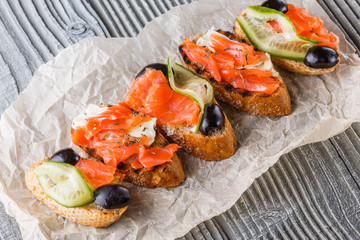 Bruschetta with smoked salmon, fresh cucumber, black olives and camembert on crumpled baking paper