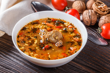 Georgian soup. Kharcho with rice, tomato, beef, garlic and herbs in bowl on wooden table