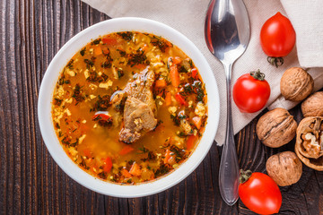Georgian soup. Kharcho with rice, tomato, beef, garlic and herbs in bowl on wooden table