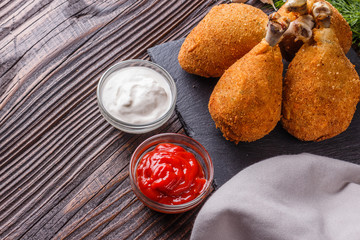 fried chicken leg in batter, red and white sauce on a dark surface