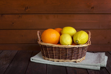 Wicker basket with fresh ripe oranges and lemons on aged wooden table.