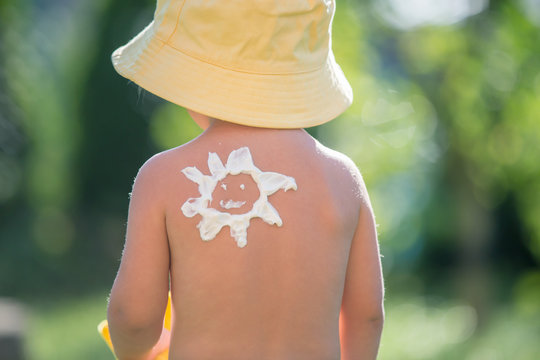 Toddler child with suntan lotion shaped as sun on his back, going at the beach with toys and flufy sun toy