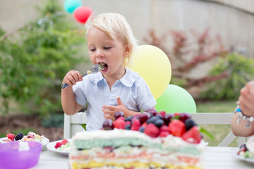 Little boy celebrating his birthday in home's garden with big cake