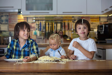 Little baby boy, toddler child and his older brothers, eating spaghetti for lunch and making a mess