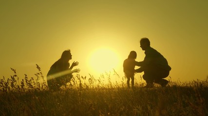 Naklejka na ściany i meble Little daughter with parents jumping at sunset. Silhouettes of mom dad and baby in the rays of dawn. Family concept. Walking with a small child in nature