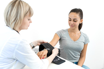 Professional female doctor putting on device for measuring pressure on young female patient hand in hospital room