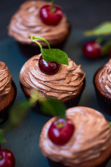 Chocolate cupcakes with ripe red cherries on dark wooden background. Selective focus. Unhealthy food