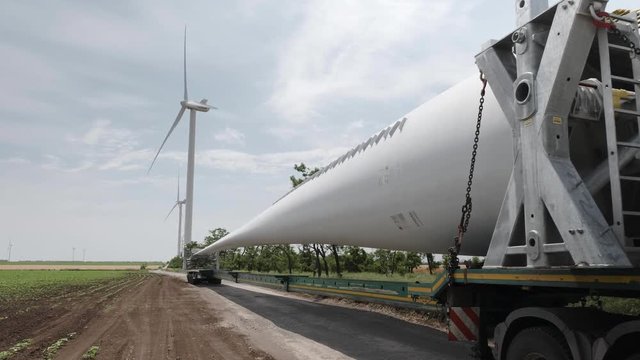 The blades of wind generators mounted on the body of long-length cargo cars against the background of the existing farm of wind power plants.