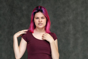 Obraz premium Portrait to the waist of a young pretty girl teenager in a burgundy T-shirt with beautiful purple hair on a gray background in the studio. Talking, smiling, showing hands with emotions.
