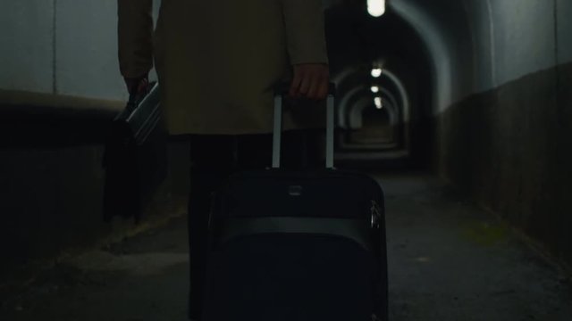 Low-section shot of man with case and rolling bag going through the dark tunnel