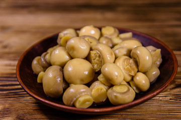 Ceramic plate with canned mushrooms on wooden table