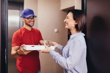 Smiling young woman receiving pizza from delivery man at home.