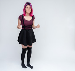Full-length portrait of young pretty teenager girl in burgundy T-shirt and black dress with beautiful purple hair on a white background in the studio. Talking, smiling, showing hands with emotions.