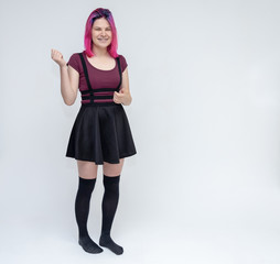 Full-length portrait of young pretty teenager girl in burgundy T-shirt and black dress with beautiful purple hair on a white background in the studio. Talking, smiling, showing hands with emotions.