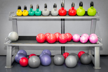 Colorful kettlebells weights and fitness ball in a row on gym floor.