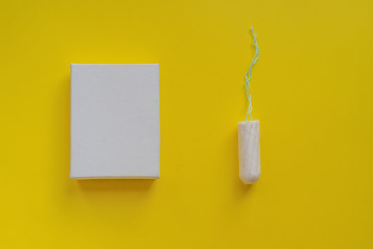 Menstrual period concept. Woman hygiene protection. Cotton tampon  in a white boxon on yellow background. Copy space and mockup
